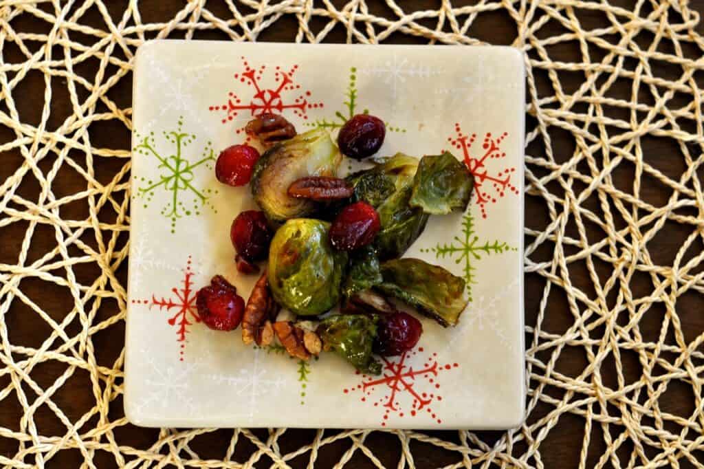 Roasted Brussels Sprouts with Cranberries and Pecans on a small square snowflake plate.