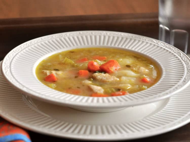 Hearty Chicken Stew served in a low bowl on a tray with orange napkin.