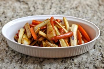 Parsnips and carrots are honey roasted and served in an oval ceramic dish.
