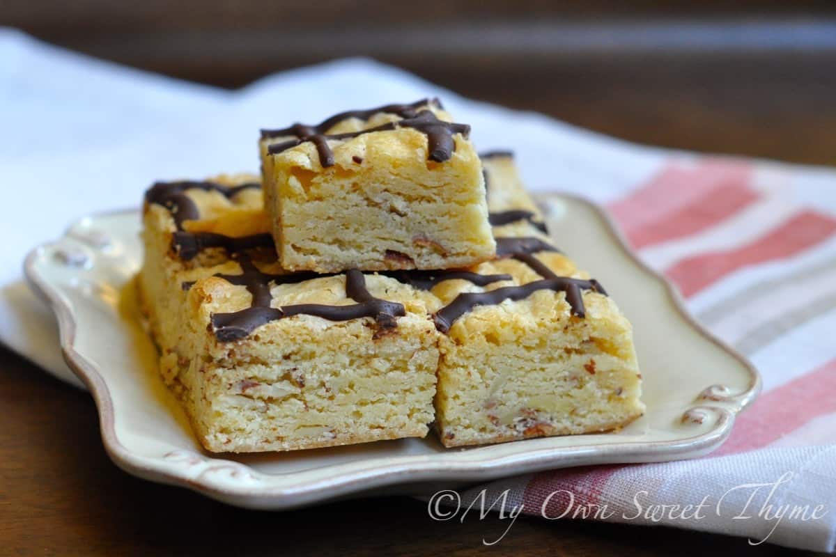 White Chocolate Almond Brownies (Blondies) drizzled with dark chocolate and stacked on a square plate