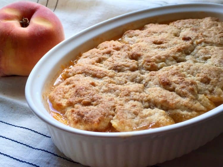 Peach Cobbler for Two on a window sill beside a ripe peach.