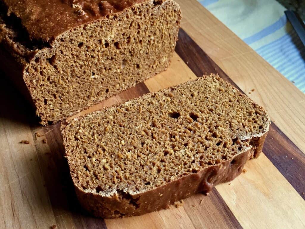 A loaf of Whole Wheat Molasses Bread is sliced open on a wooden cutting board.