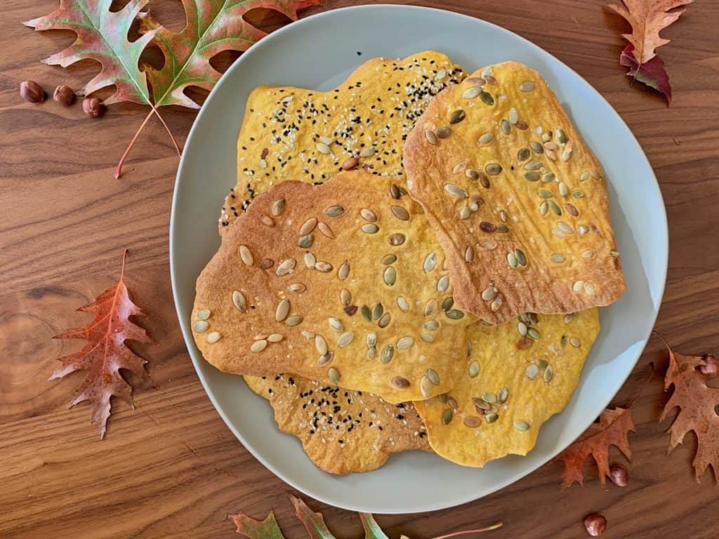 Pumpkin Sourdough Crackers on a ceramic plate surrounded by fall leaves.