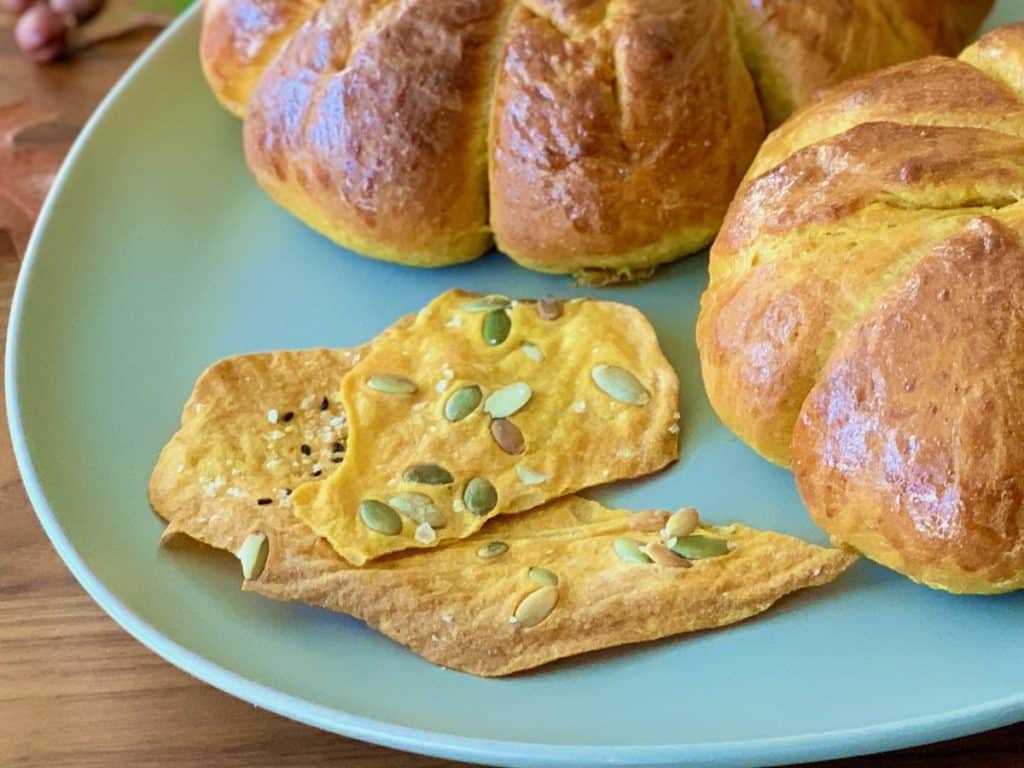 Pumpkin Sourdough Cracker Leaves beside loaves of pumpkin shaped loaves of Pumpkin Yeast Bread on a green plate.