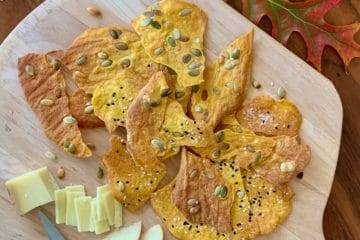 Pumpkin Sourdough Crackers on a board with cheese and apples surrounded by fall leaves