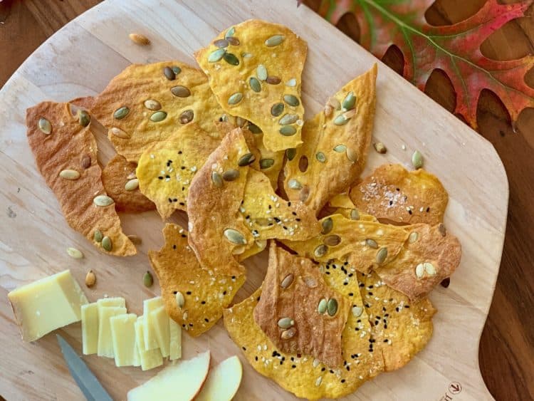 Pumpkin Sourdough Crackers on a board with cheese and apples surrounded by fall leaves