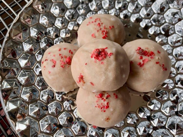 Pfeffernüsse topped with crushed pink peppercorns are stacked on a silvered dessert plate.