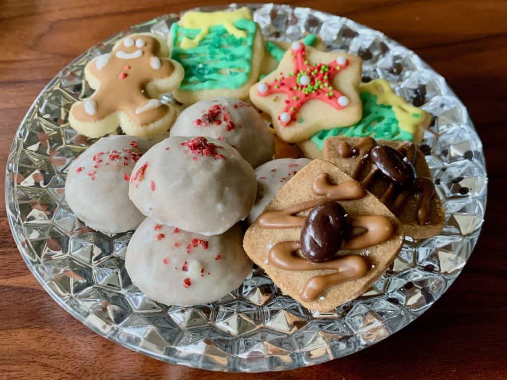 An assortment of Christmas cookies including pfeffernüsse, Coffee Crisps, and decorated Sugar Cookies arranged on a silvered glass plate.