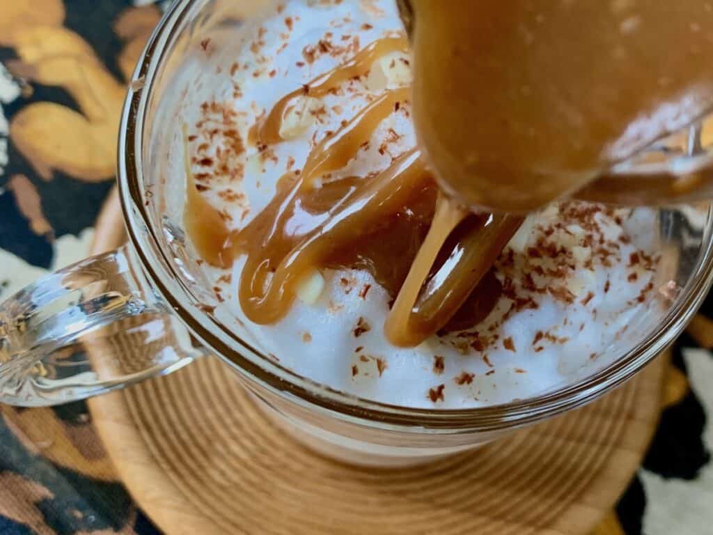 A drizzle of soft Peanut Butter Fudge tops a delicious latte in a clear glass cup.