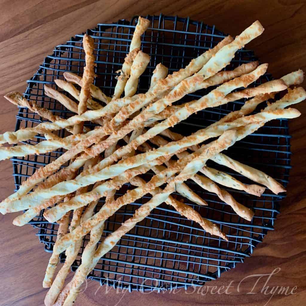 Sourdough breadsticks with parmesan cheese and rosemary on a black wire rack.