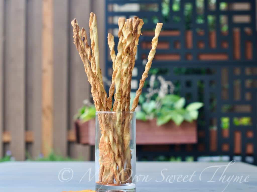 Thin, crispy breadsticks arranged in a glass on an outdoor table.