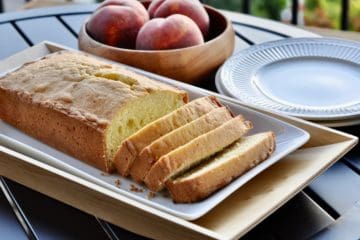 A loaf of old fashioned pound cake cut into thick golden slices and served with a bowl of peaches