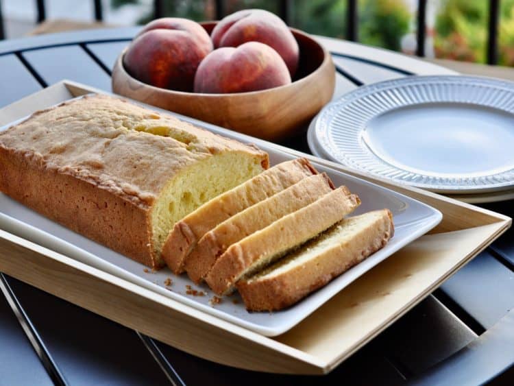 A loaf of old fashioned pound cake cut into thick golden slices and served with a bowl of peaches