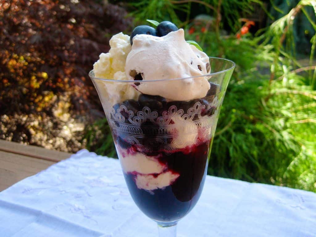 Summer Berry Basil Sauce layered with Meringue Cookie to make a simple parfait served in a pretty wine glass.