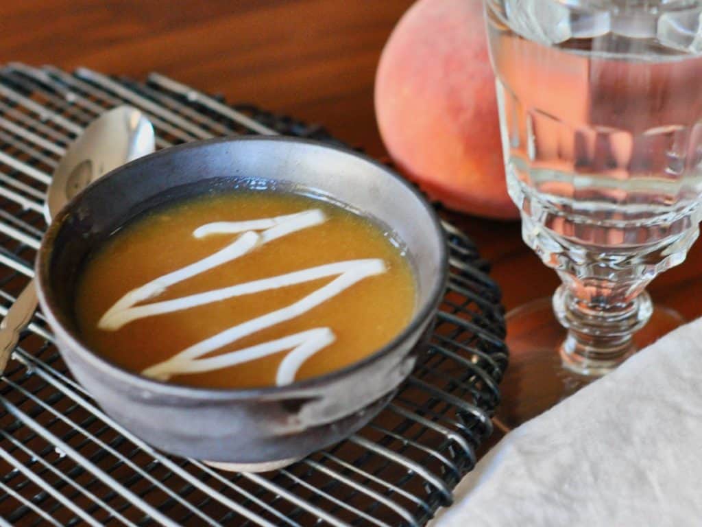 Cold Peach Soup garnished with whipped cream in a small bowl set on a wire rack