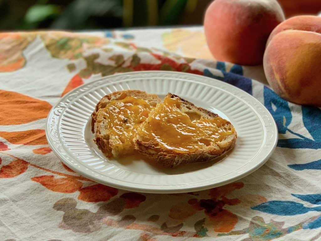 Peach Butter Spread on Sourdough Toast and served on a saucer beside ripe peaches.