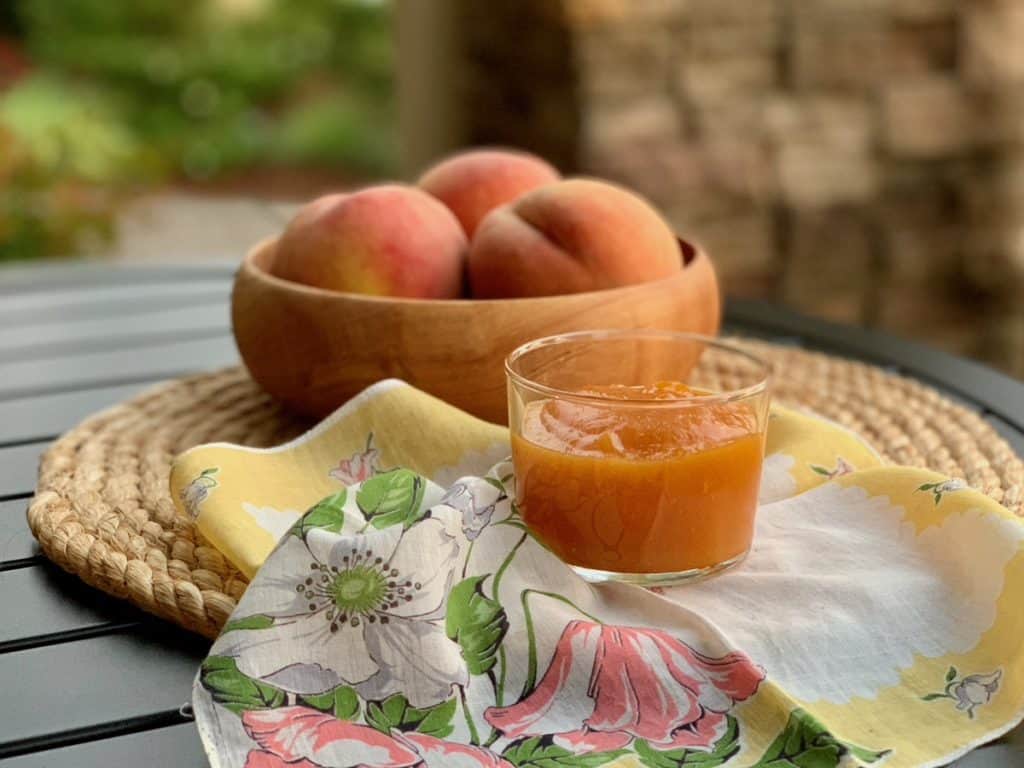 A dish of peach butter on a table set with an antique napkin and a rope placemat