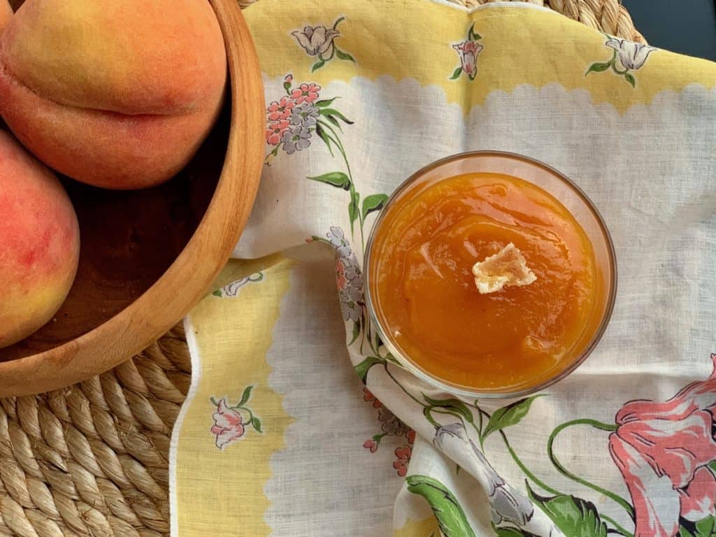 A glass dish filled with Peach Butter on an antique yellow napkin.