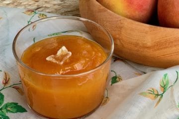 Peach Butter topped with a slice of crystallized ginger in a glass dish beside a wooden bowl.