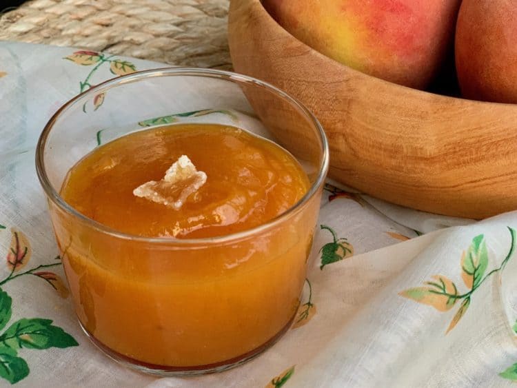 Peach Butter topped with a slice of crystallized ginger in a glass dish beside a wooden bowl.