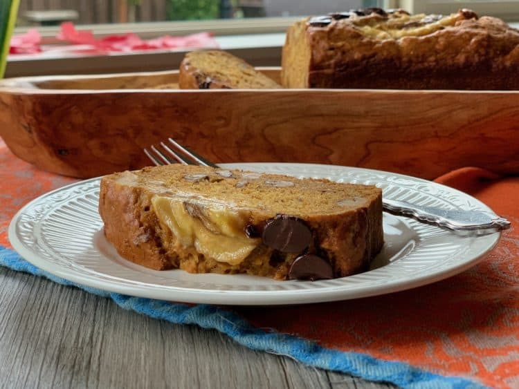 A slice of Banana Pumpkin Bread on a plate in front of the cut loaf on a wood platter.