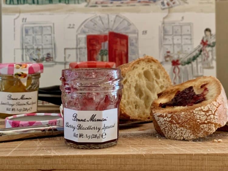 Several jars of fruit spreads on a wooden cutting board with slices of Sourdough Bread with a Bonne Mama advent calendar in the background.