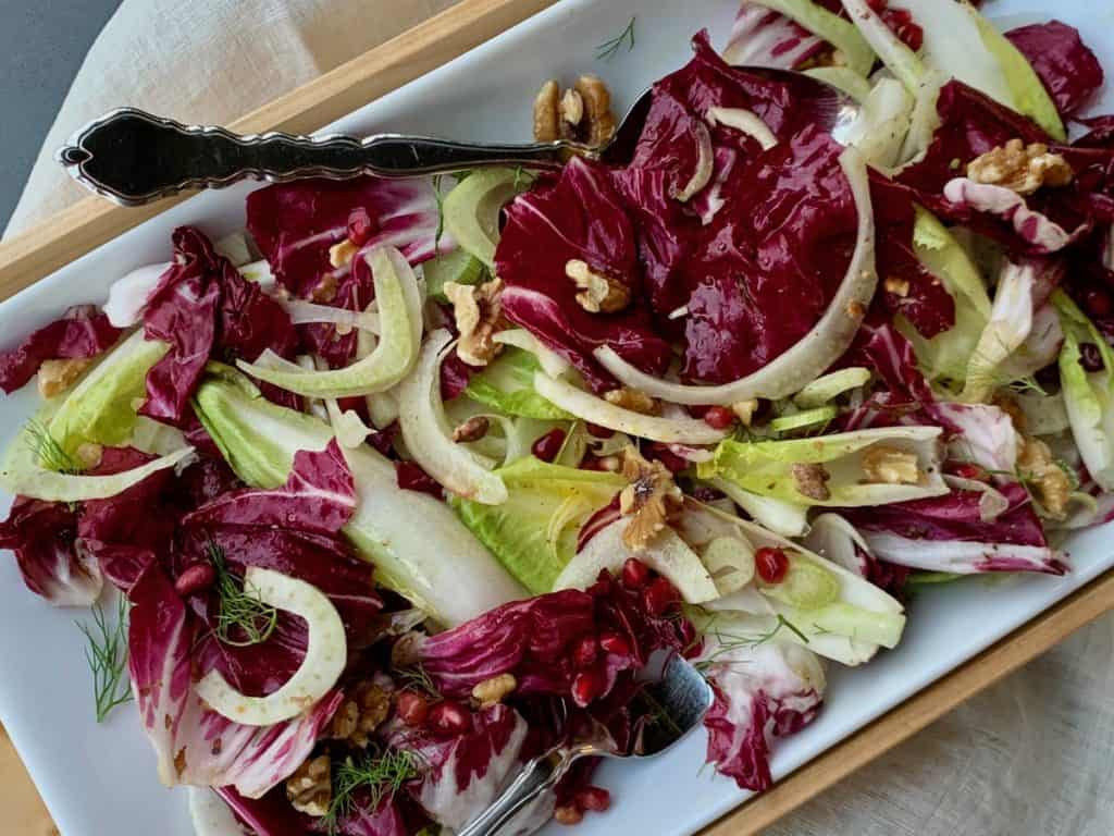 Festive Endive Salad is composed of fennel, radicchio, endive, walnuts and pomegranate arils in a simple dressing served from a rectangular platter.