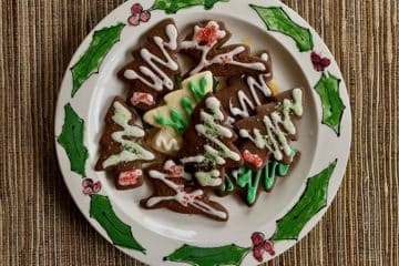 Ginger and Spice Cutout Cookies decorated with Vanilla Icing arranged on a plate decorated with holly leaves.