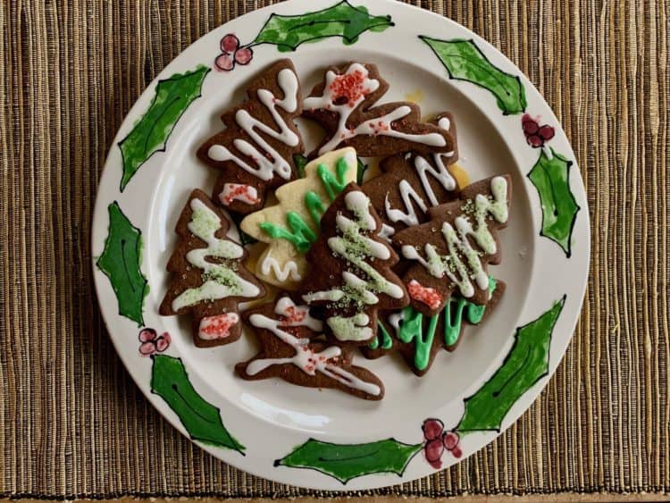 Ginger and Spice Cutout Cookies decorated with Vanilla Icing arranged on a plate decorated with holly leaves.