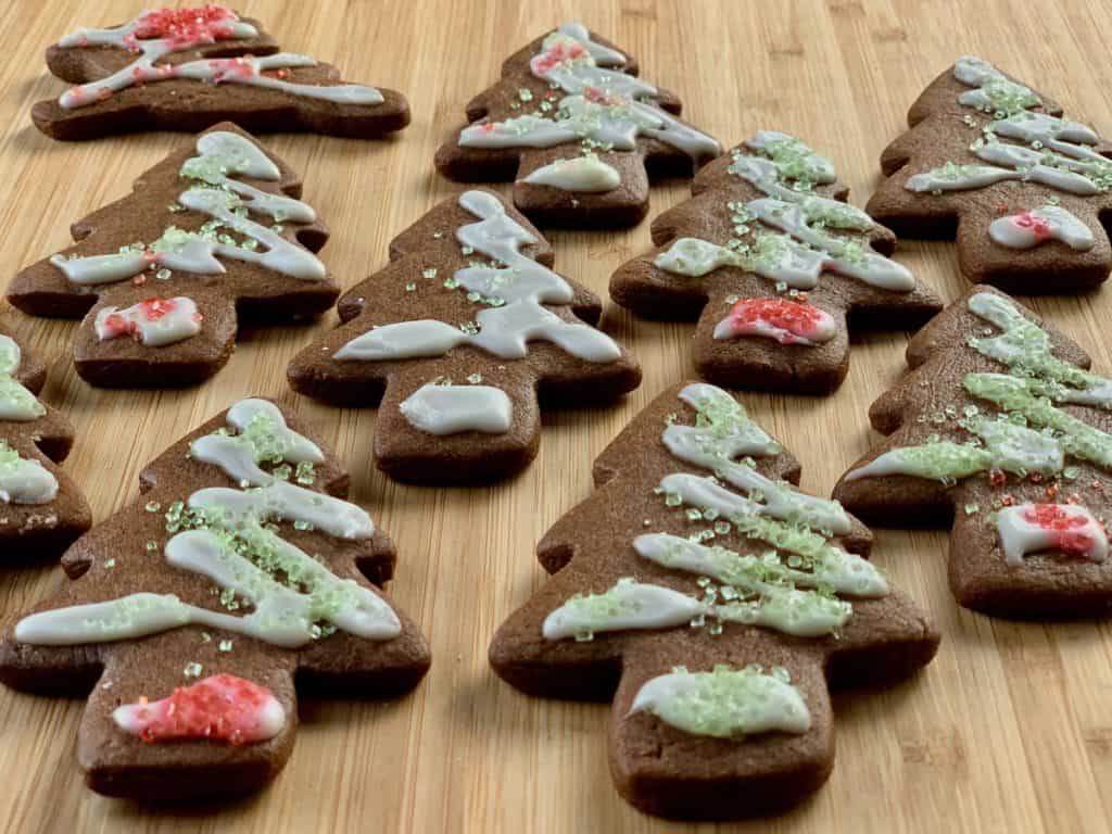 Ginger and Spice Cutout Cookies, dark with molasses and cocoa powder, decorated with Vanilla Icing Drizzle and colored sugar laid out on a butcher block board.