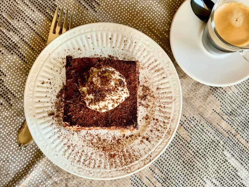Simple Tiramisu with whipped cream and a dusting of cocoa powder served on a dessert plate with a cup of coffee.