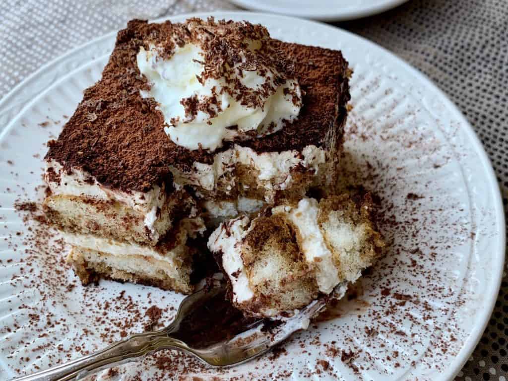 A slice of Simple Tiramisu topped with Whipped Cream and grated chocolate served on a plate with one bite held on a fork. 