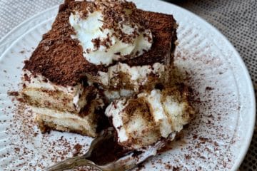 A slice of Simple Tiramisu topped with Whipped Cream and grated chocolate served on a plate with one bite held on a fork.