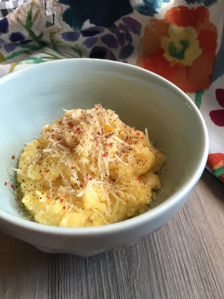 Breakfast Grits topped with pepper and Parmesan in a blue bowl with appliqué apron.