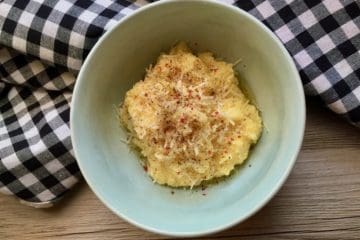 Breakfast Grits topped with pepper and Parmesan in a blue bowl beside a checked apron.