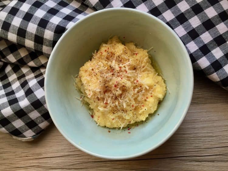Breakfast Grits topped with pepper and Parmesan in a blue bowl beside a checked apron.