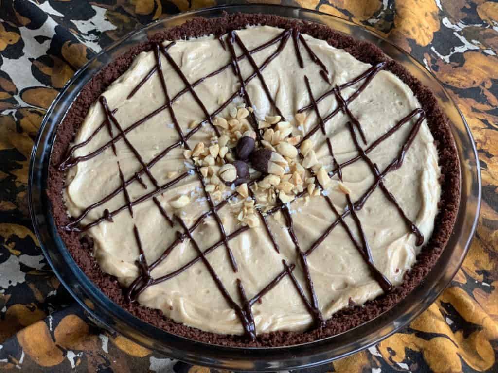 Peanut Butter Pie drizzled with chocolate, and topped with chocolate dipped peanuts and sea salt,  in a chocolate cookie crumb crust.