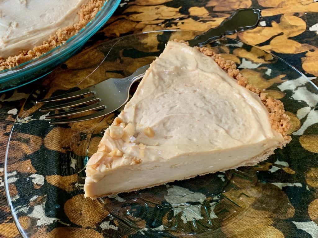 A slice of Peanut Butter Pie topped with chopped peanuts and sea salt in a graham cracker crumb crust.