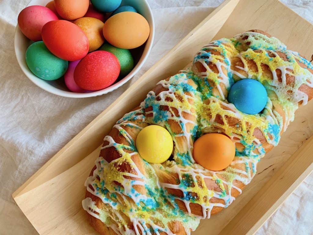 An Easter Bread Braid studded with Easter eggs beside a bowl of dyed Easter eggs.