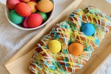 An Easter Bread Braid studded with Easter eggs beside a bowl of dyed Easter eggs.