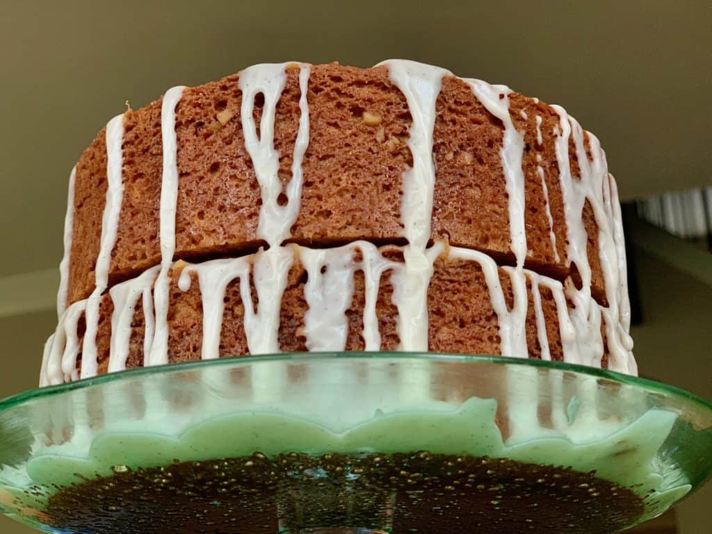 A Cinnamon Sour Cream Layer Cake with Vanilla Icing drizzled down the sides resting on a glass pedestal plate.