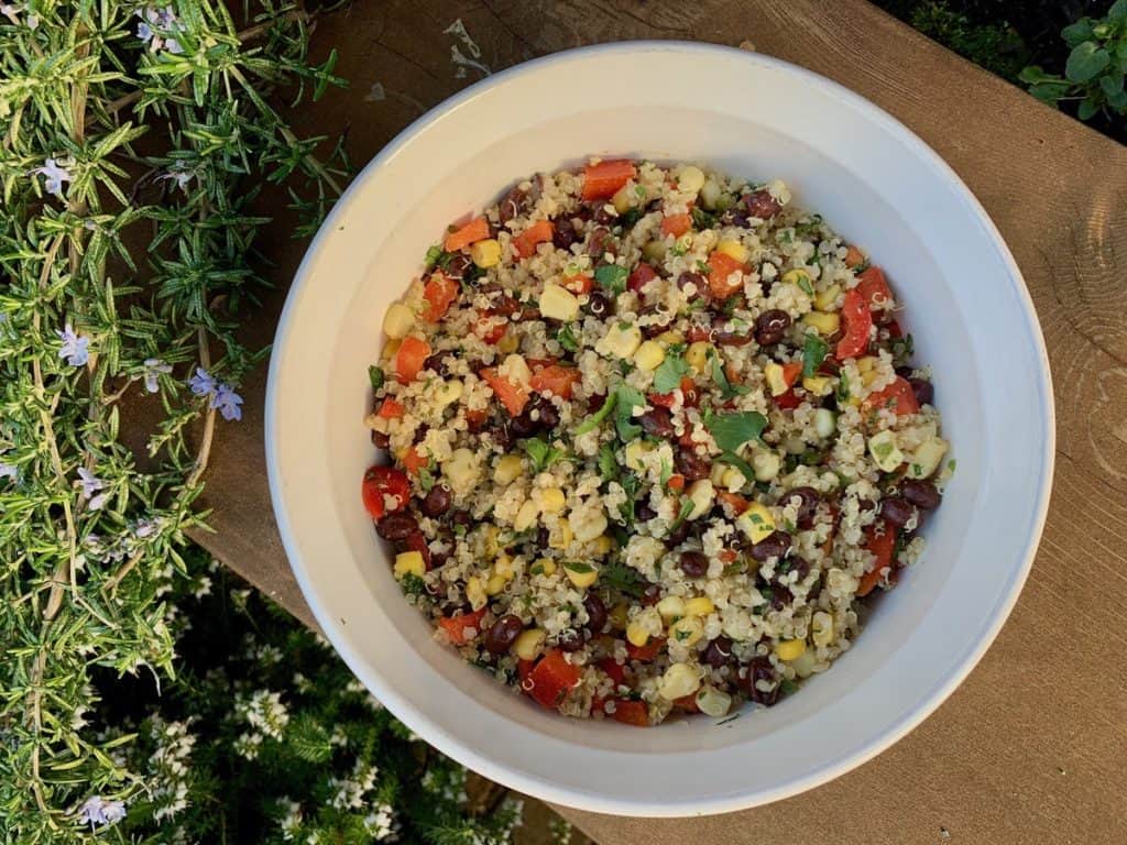 Southwest Quinoa Salad, with black beans, corn, red pepper and cilantro, in a white serving dish in the garden.
