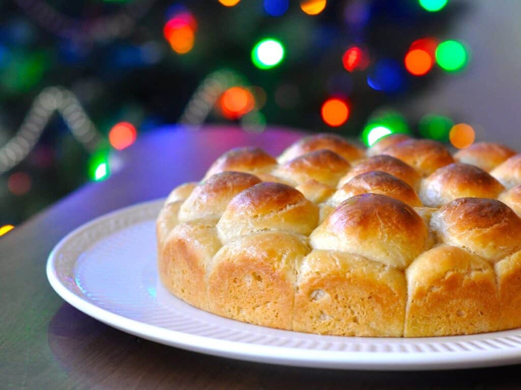 Cheese Bread formed into pull-apart rolls are served on a white platter in front of a lit Christmas Tree.