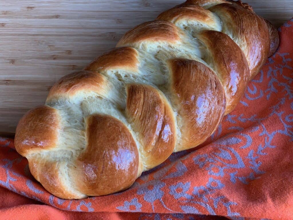 A loaf of Braided Cheese Bread on a patterned bread cloth.