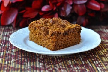 A square slice of Gingerbread Coffee Cake in front of a red Christmas Wreath.