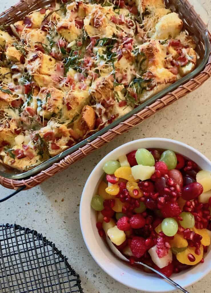 A Festive Fruit Salad served beside an Arugula and Ham Strata for a holiday breakfast.