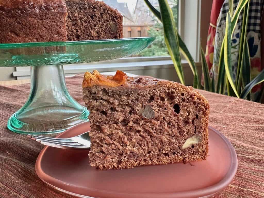 A slice of Wild Persimmon Cake served on a square glass plate with the sliced Persimmon Cake in the background.