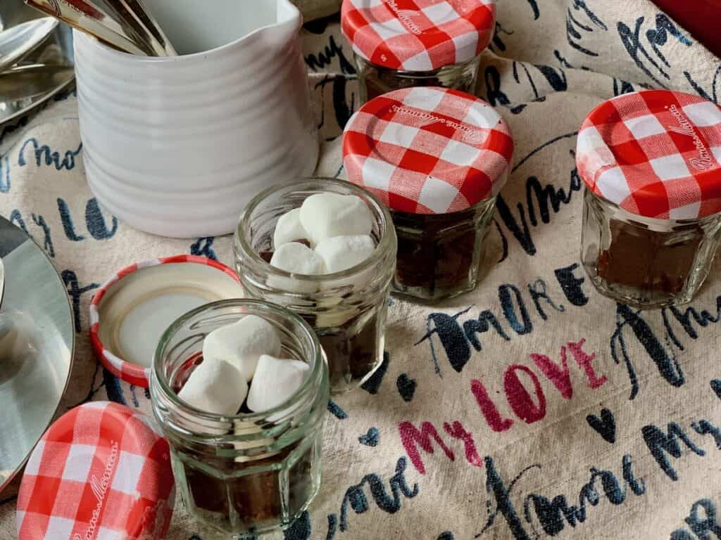 Small jars are filled with Aunt Noni's Christmas Fudge, chocolate chips and marshmallows. Just add to hot milk to make Fudgy Hot Chocolate. 