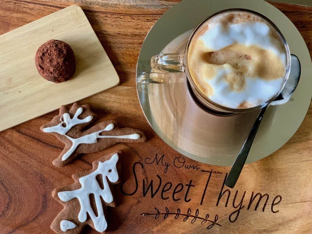 A piece of Aunt Noni's Christmas Fudge, rolled into a ball and coated with cocoa powder, is the base for this cup of hot chocolate topped with a shot of espresso served beside two Ginger Spiced Cutout Cookies. 