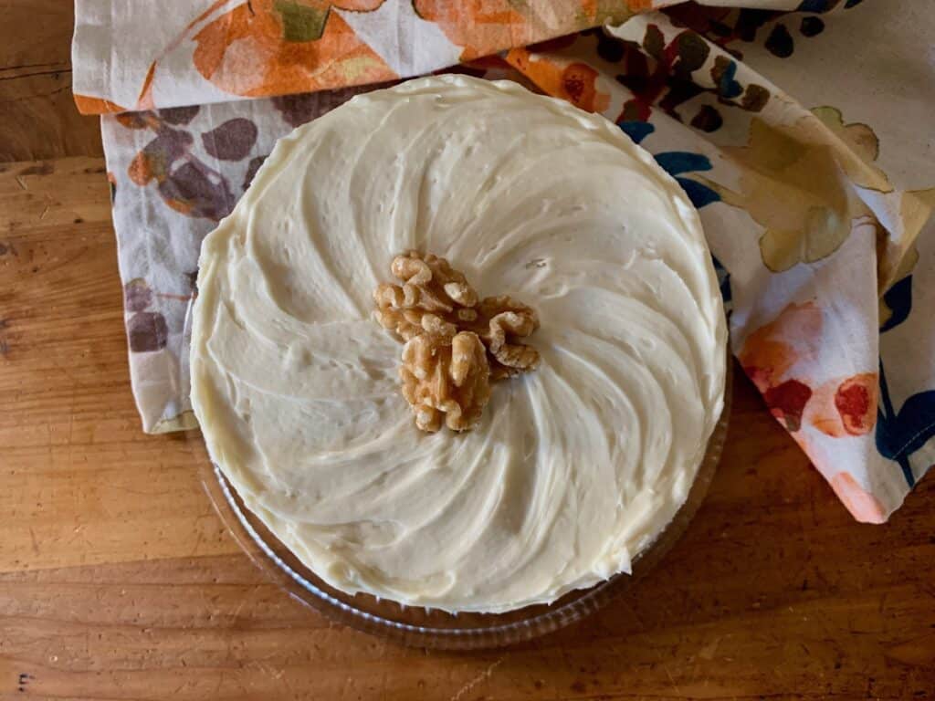 A Carrot Cake, viewed from the top, covered in Cream Cheese Frosting and topped with several walnut halves.